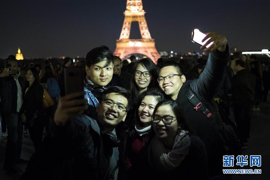 5月15日，在法国首都巴黎，游客们与正在进行声光秀的埃菲尔铁塔合影。