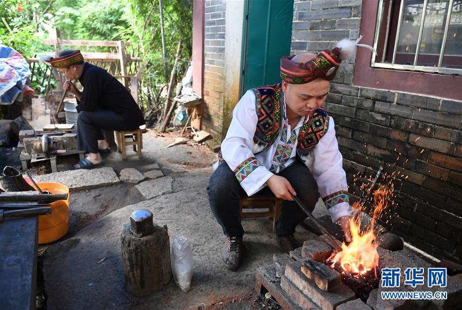 5月29日，在广西融水苗族自治县融水镇，银匠陈志元（右）在生炭火准备打造银饰。