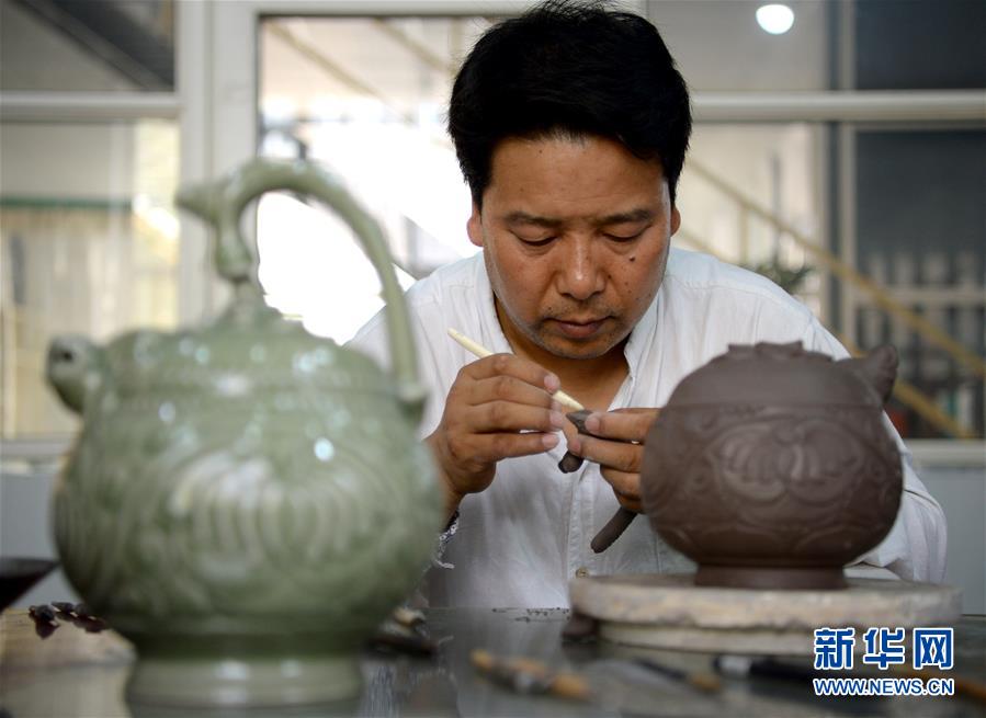崔涛在对手工制作的耀州窑青釉剔花倒装壶进行刻花。