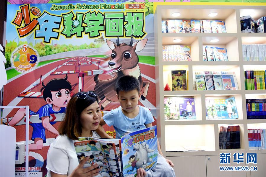 7月17日，一名家长在童书博览会上给孩子讲解图书内容。
